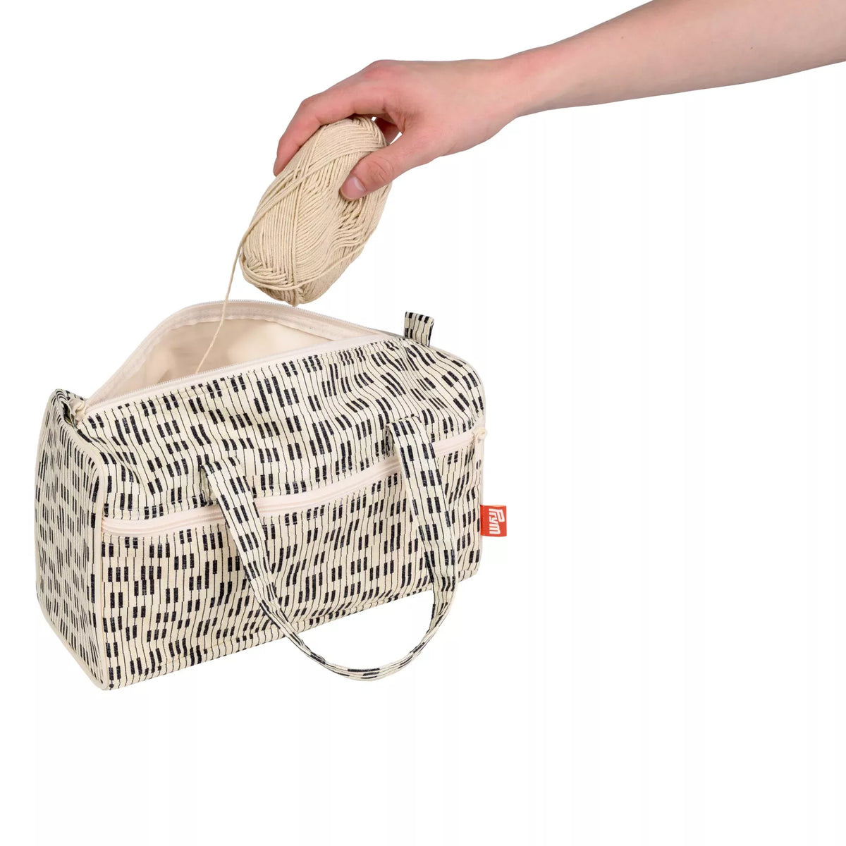 Prym Piano project bag in cream and black with a ball of wool being placed inside.