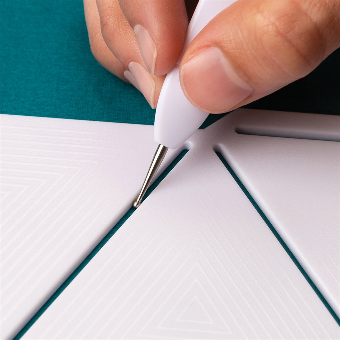 A hand uses a scoring tool on a white papercraft template with triangular sections.