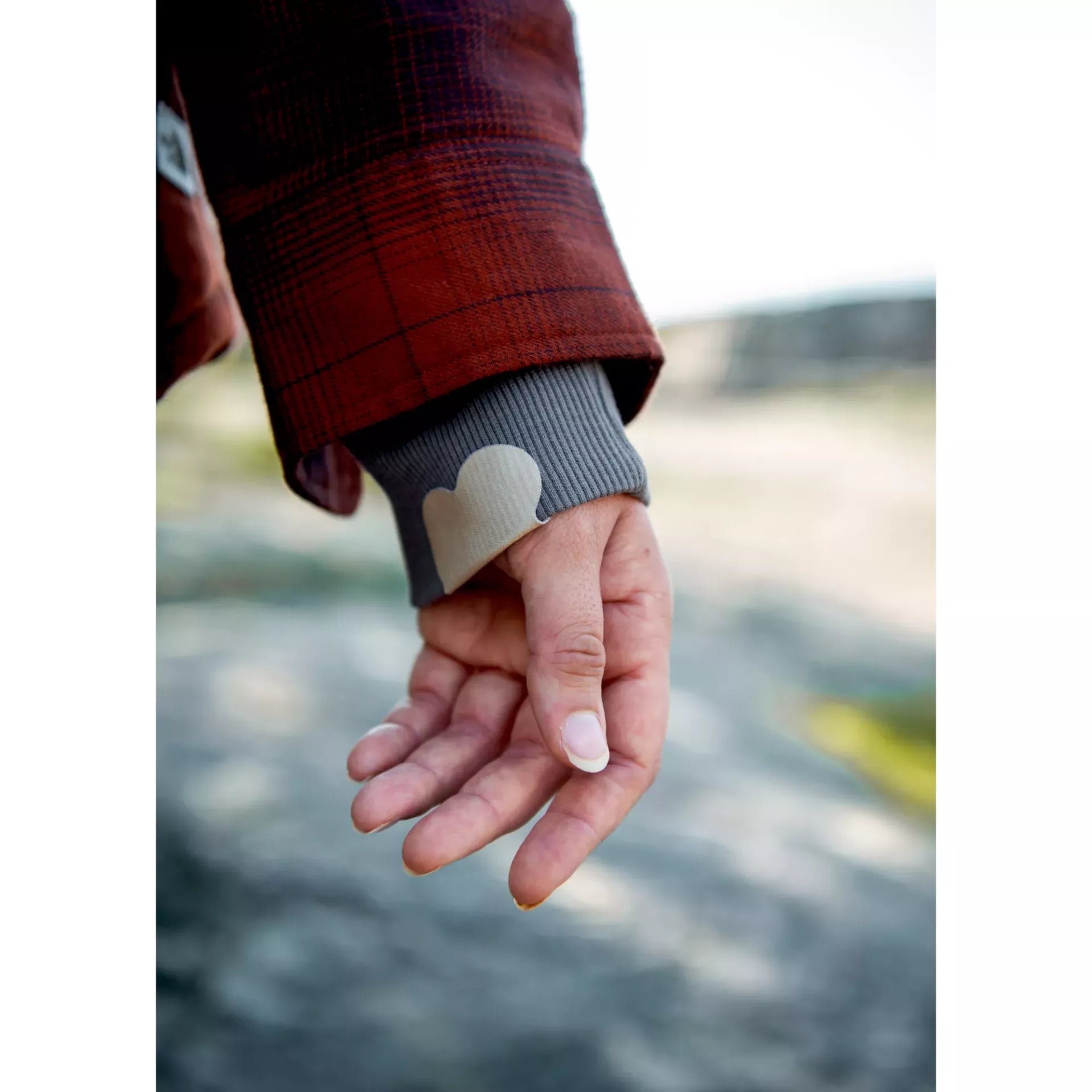 A person wearing a red plaid jacket with a heart-shaped Prym rub-on stretch patch on the grey cuff.
