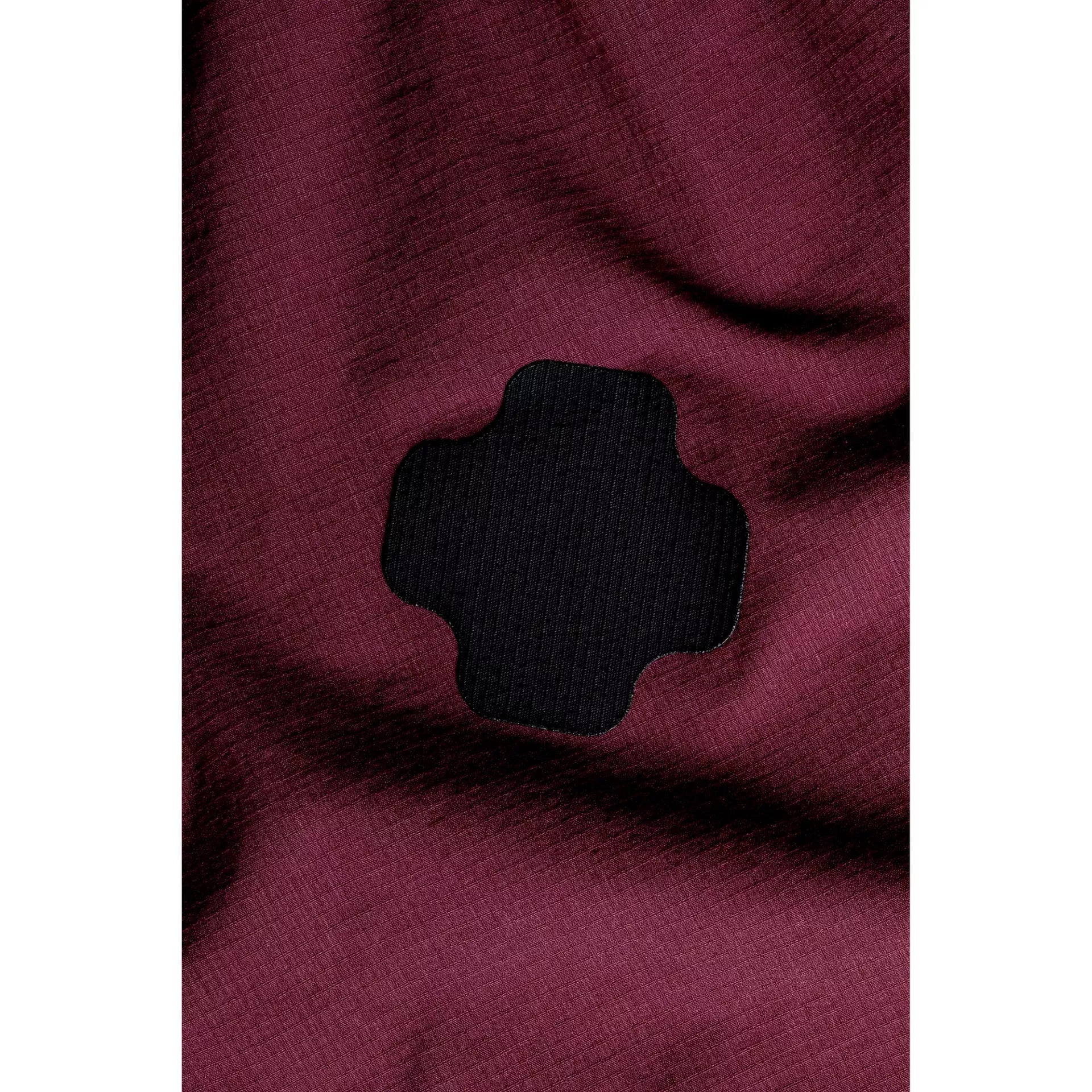 Close-up of a black, cross-shaped Fabpatch Extreme waterproof repair patch on maroon fabric.
