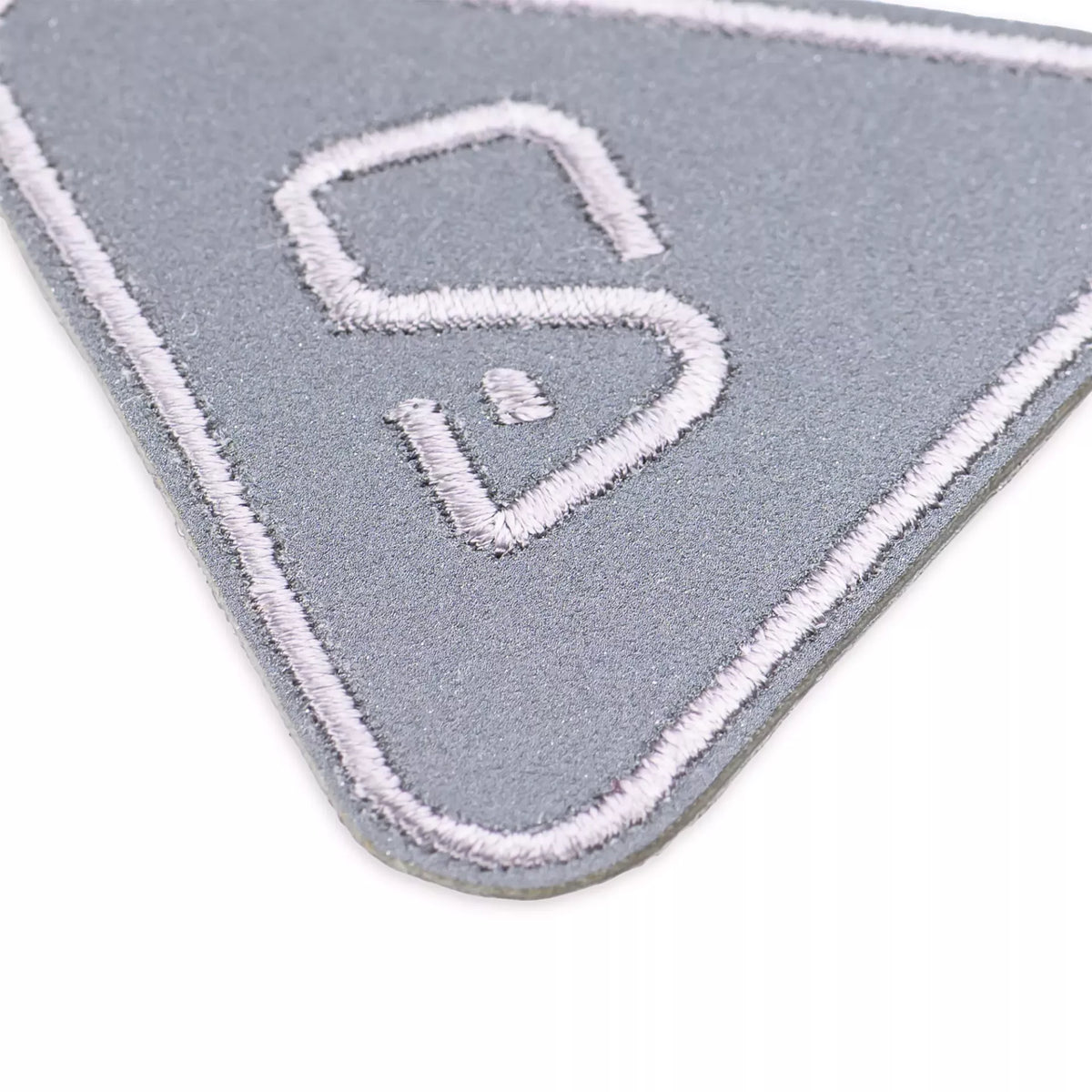 Close-up of a grey reflective triangle appliqué with white embroidered border and central S design.