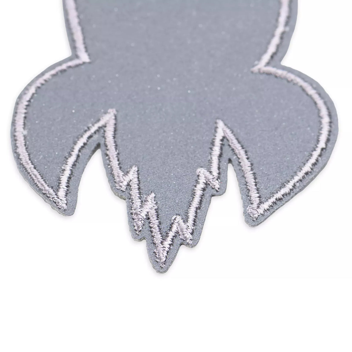 Close-up of a grey reflective rocket appliqué with white embroidered edges.