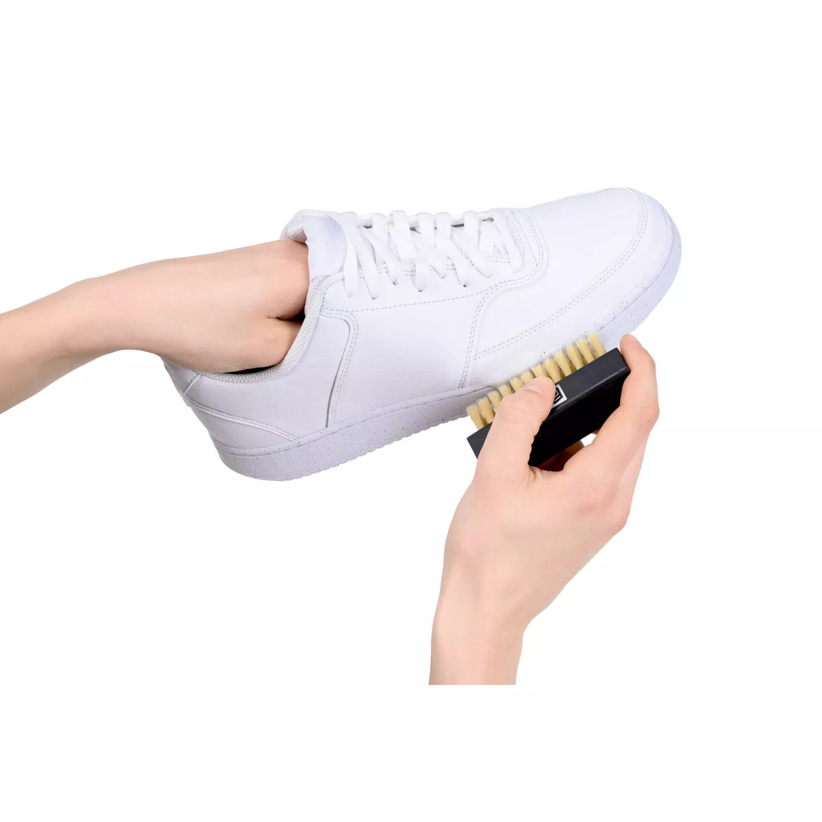 Person using a black brush to clean a white leather sneaker from the sneaker care set.