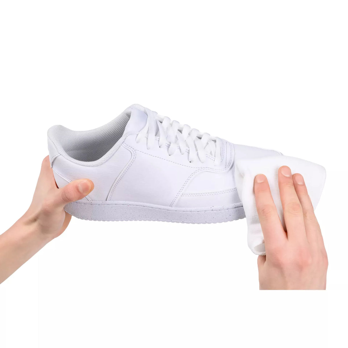 Hands using a white microfiber cloth to clean a white leather sneaker.