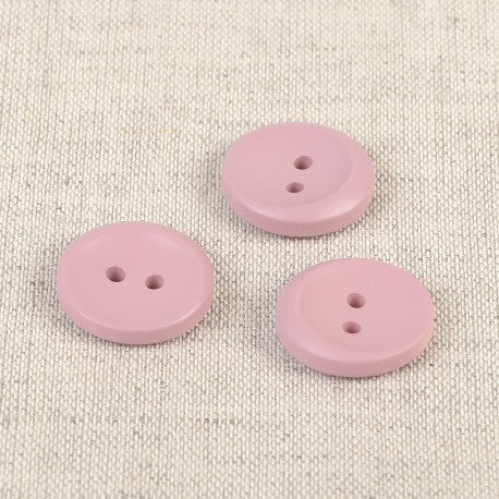 Three 17mm round pink plastic sewing buttons with two holes on a textured fabric background.