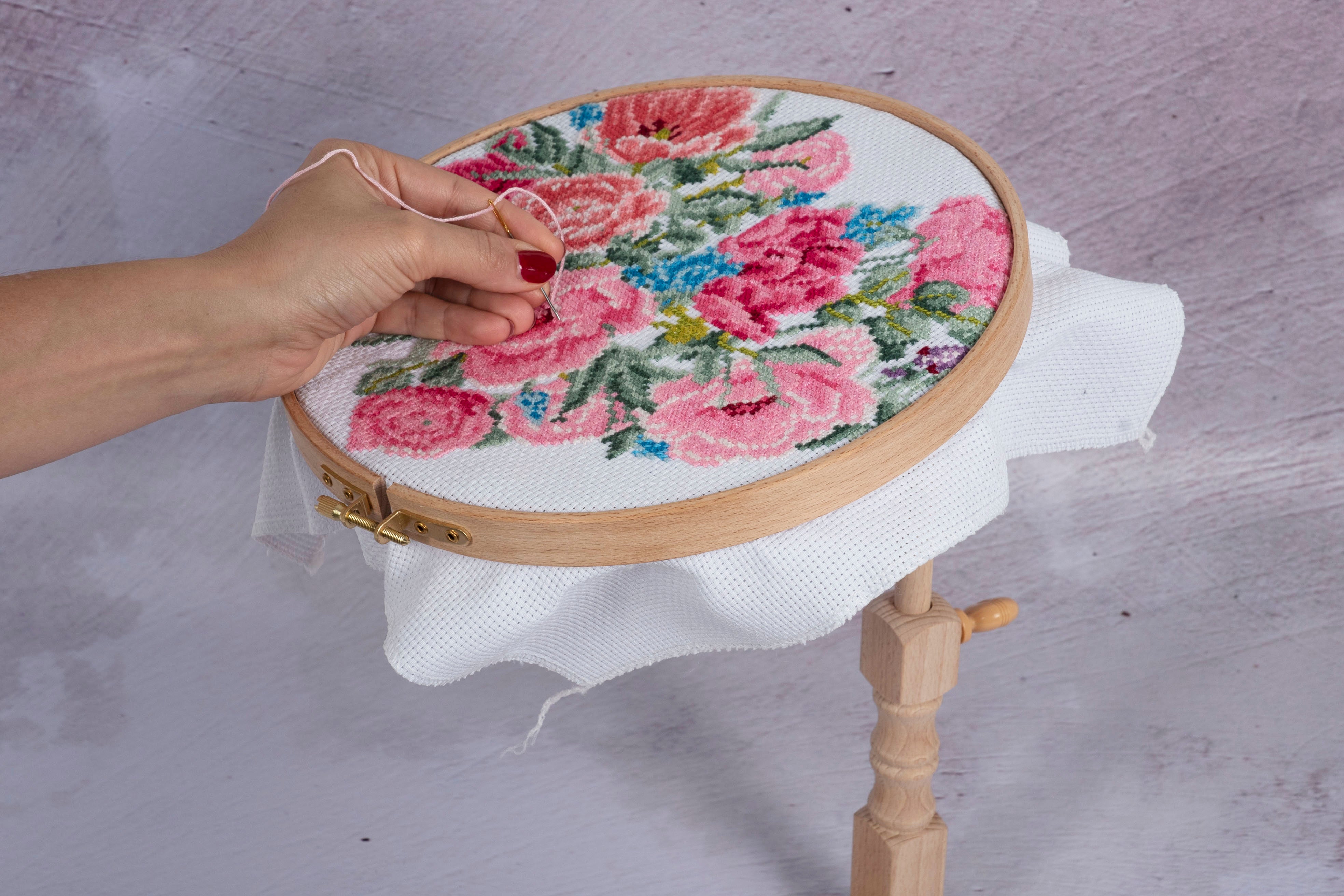 Hand stitching a floral cross-stitch pattern on a beech wood seat frame embroidery hoop.
