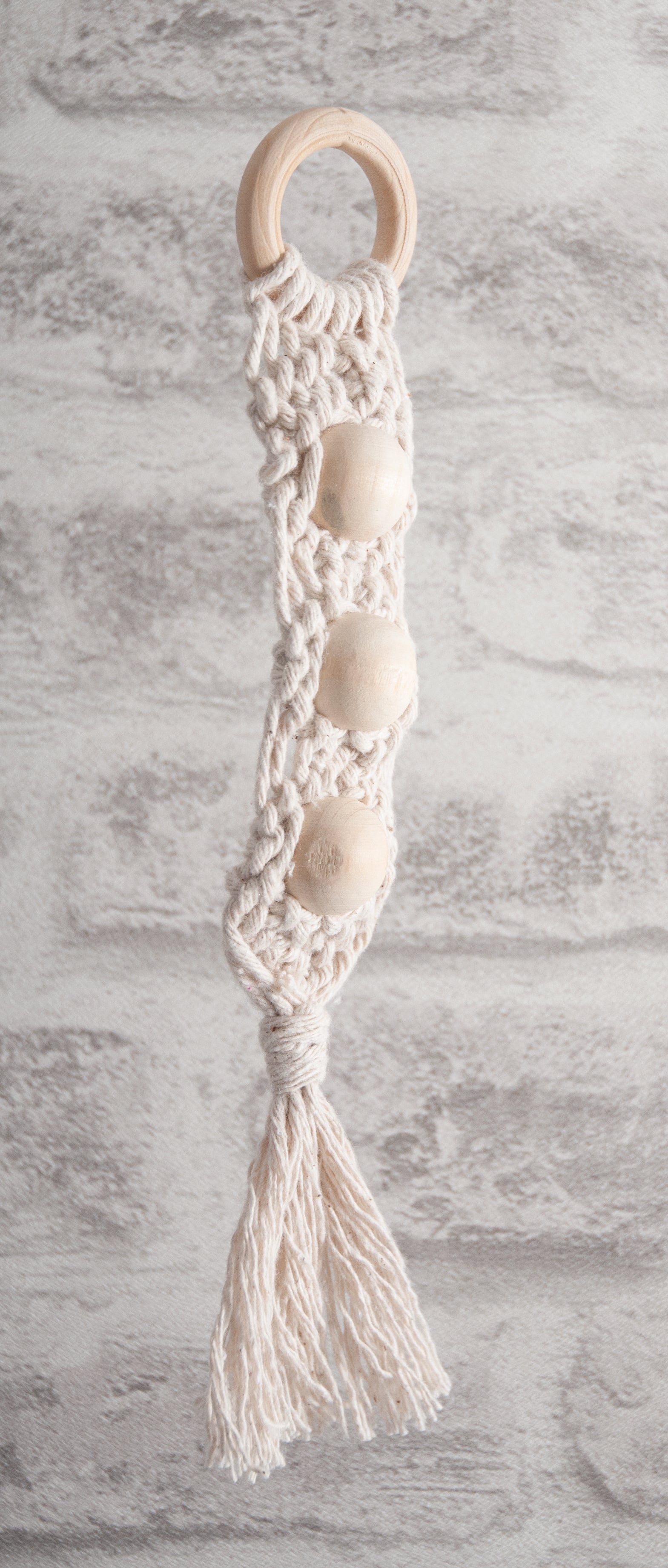 Three large round wooden beads woven into a cream macrame wall hanging with a wooden ring.