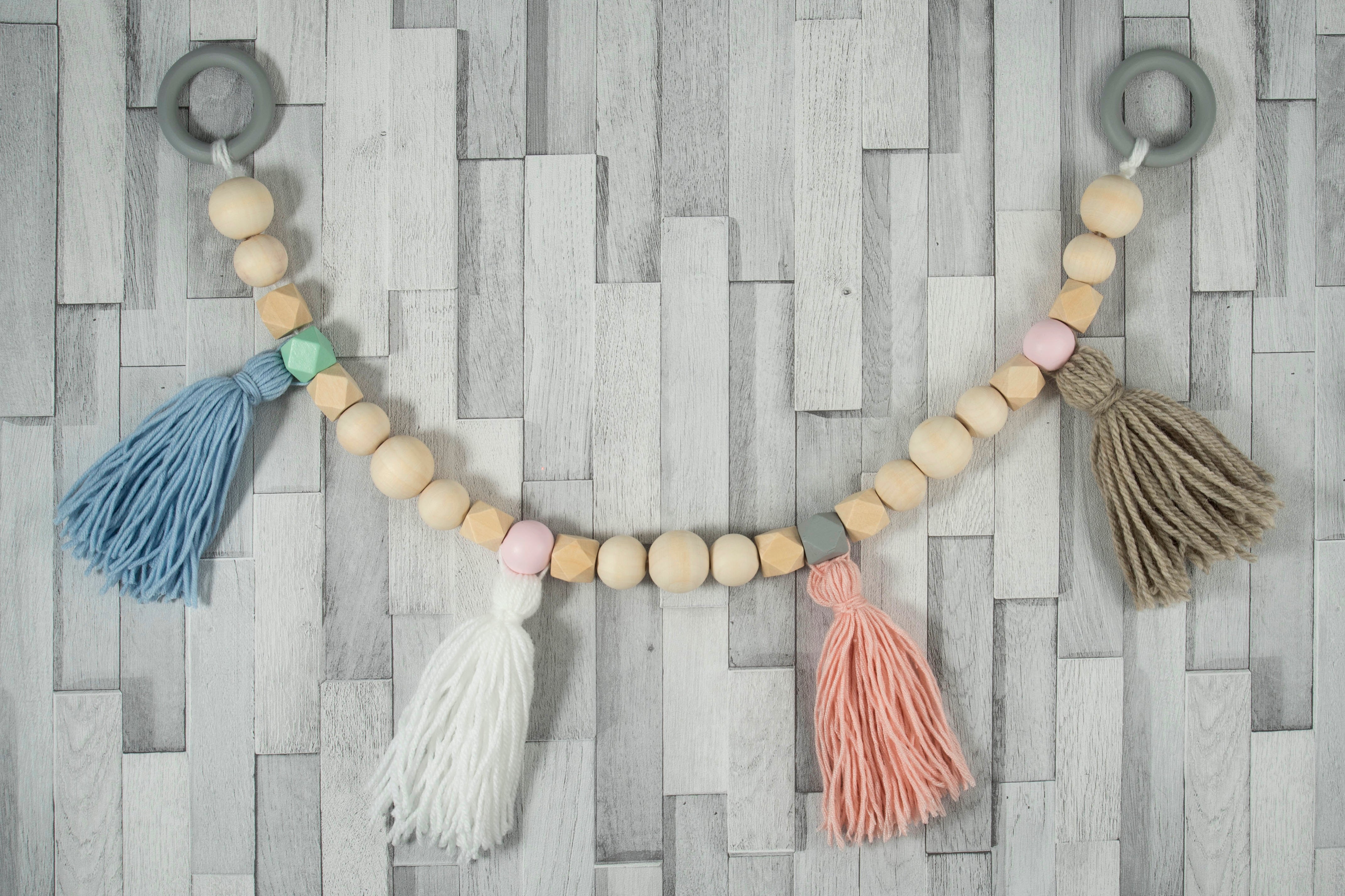 A decorative garland made of natural and pastel wooden beads with colorful yarn tassels.
