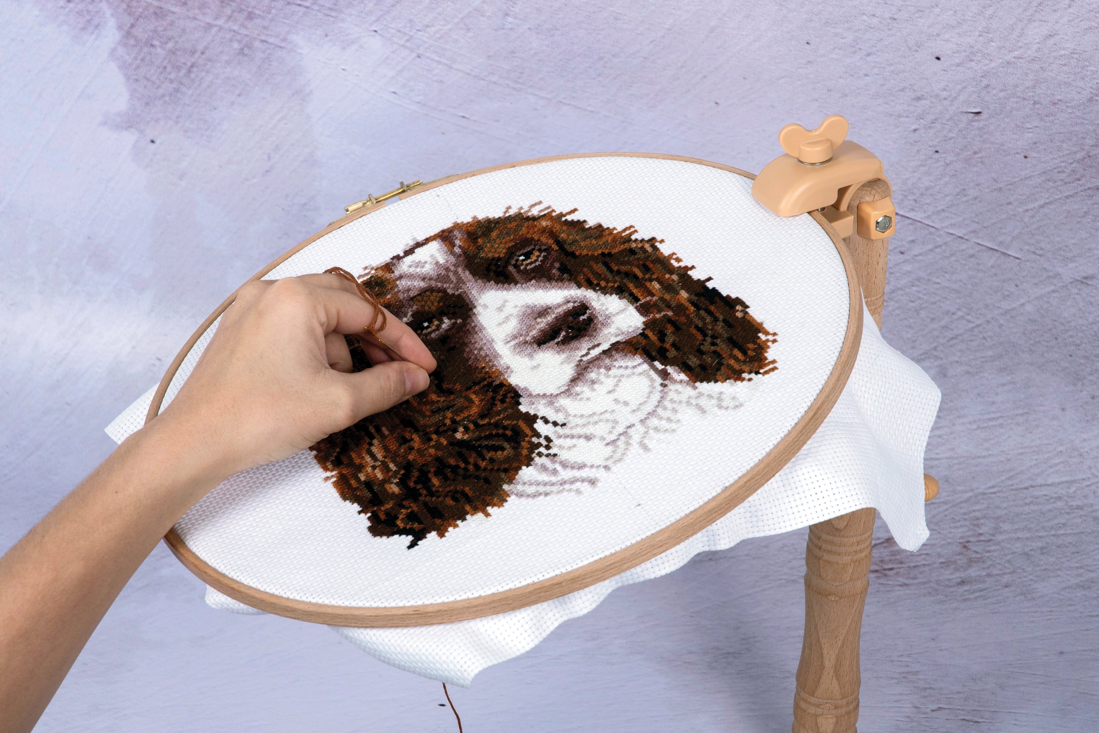 A person using a Milward beech wood table clamp to hold an embroidery hoop with a dog design.