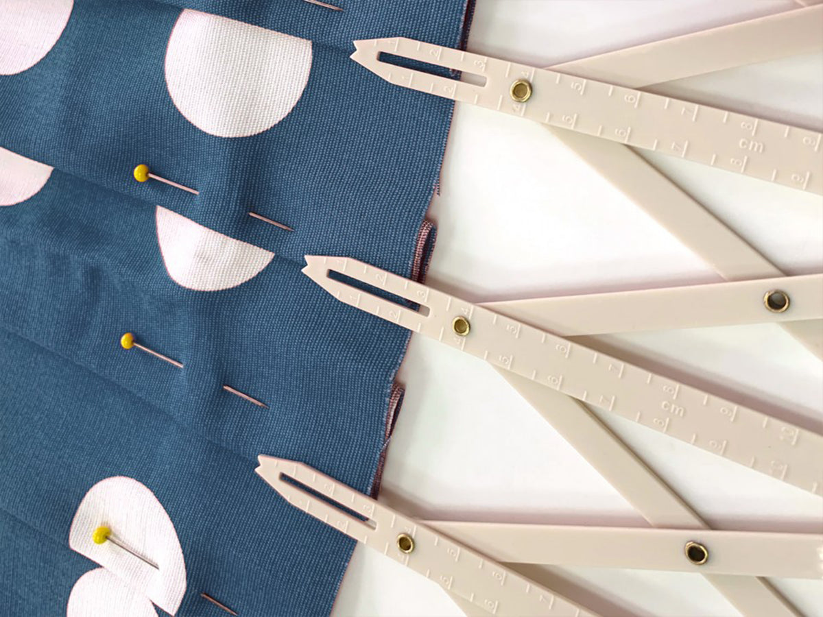 Expandable plastic sewing gauge with cm and inch markings used to measure pleats on blue fabric.