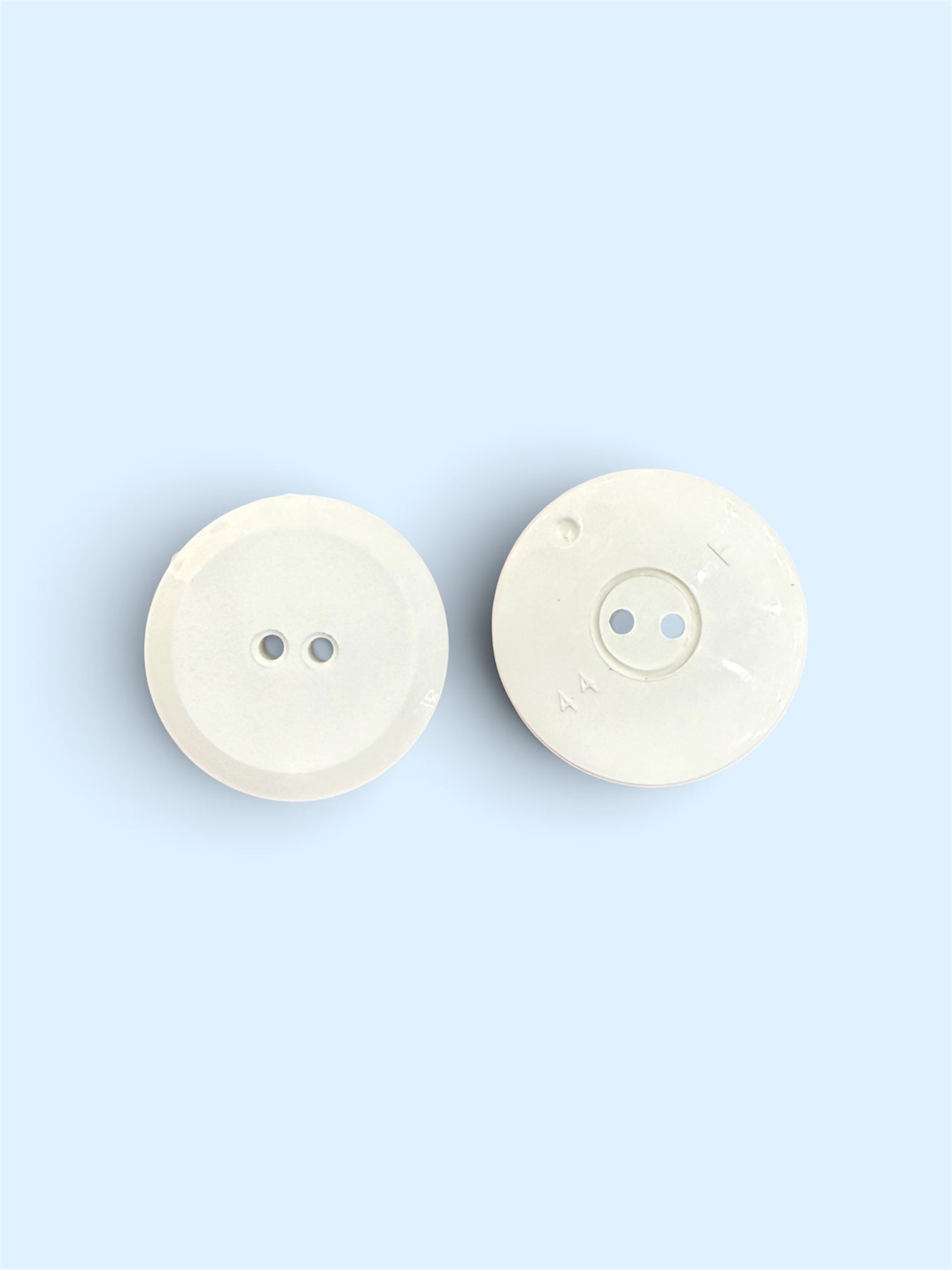 Two 24mm white resin flat buttons with a 2-hole design on a light blue background.