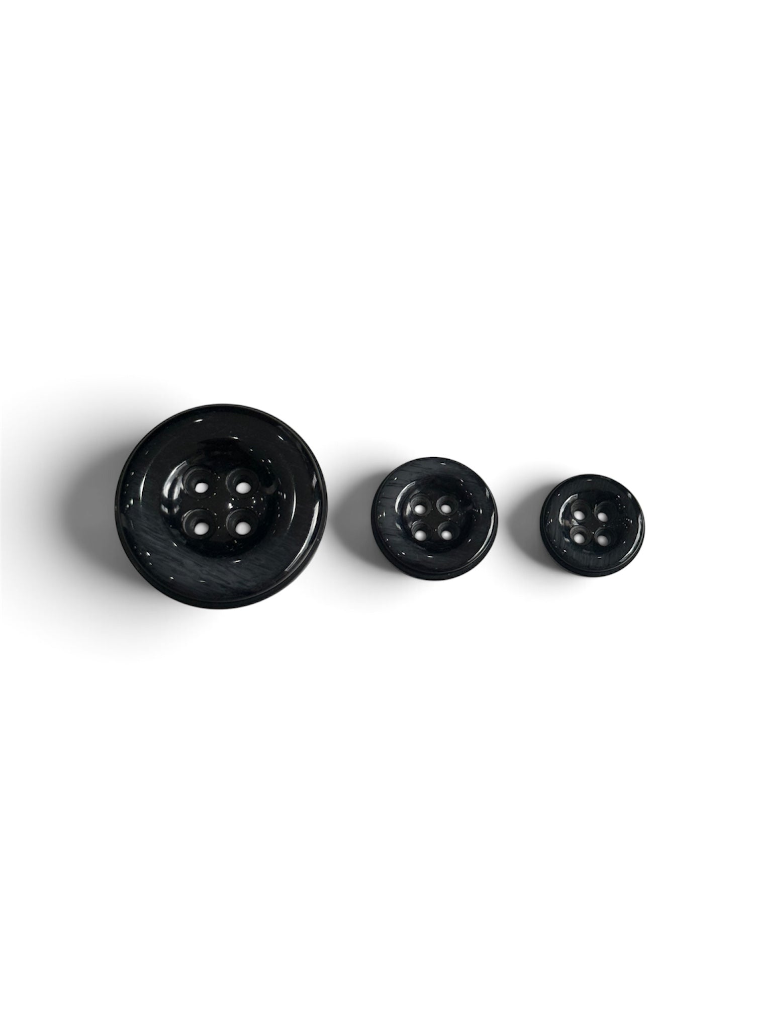 Three black resin 4-hole round sewing buttons in varying sizes on a white background.