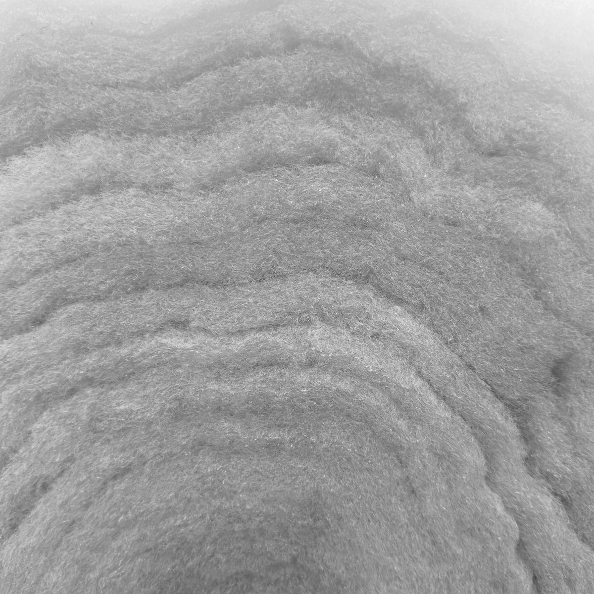 Close-up of white thick polyester wadding showing its soft, fibrous texture and high-loft layers.