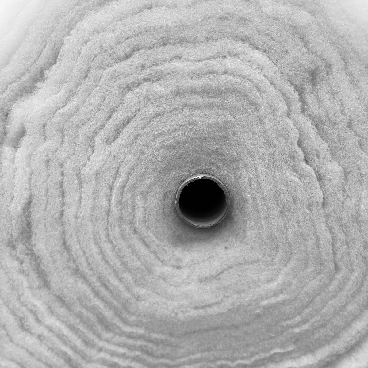 Close-up cross-section of a roll of white thick polyester wadding quilting batting.