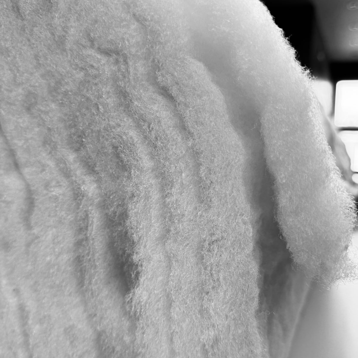 Close-up of white thick polyester wadding showing its soft, high-loft fibrous texture.