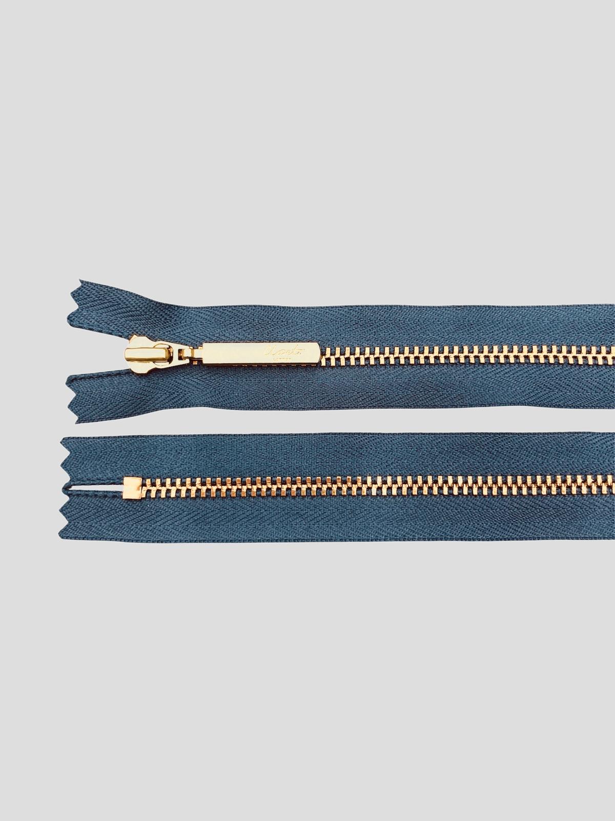 YKK size 3 closed end gold metal zipper on dark teal fabric.