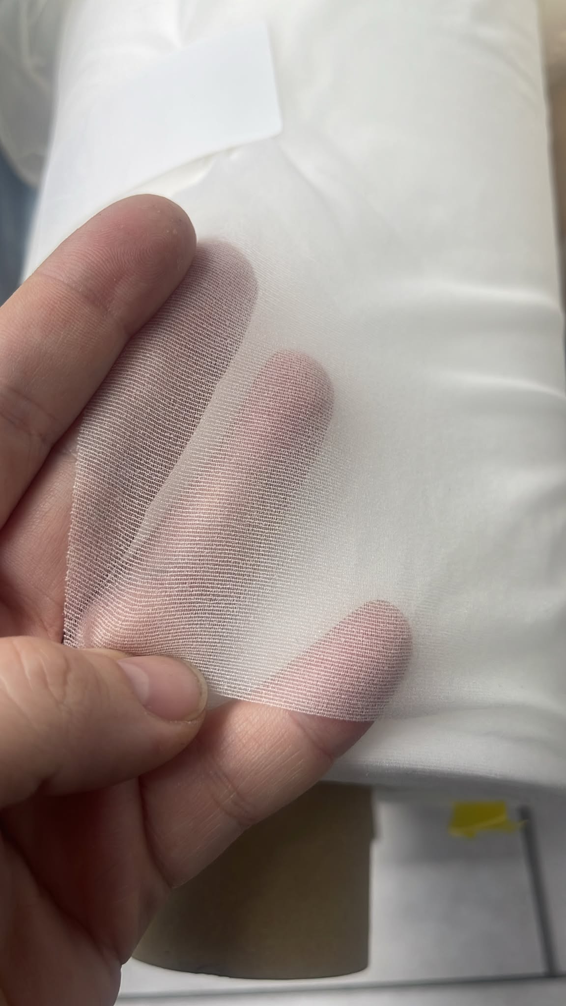 Close-up of white XR woven fusible interlining fabric held by a hand to show its sheer texture.