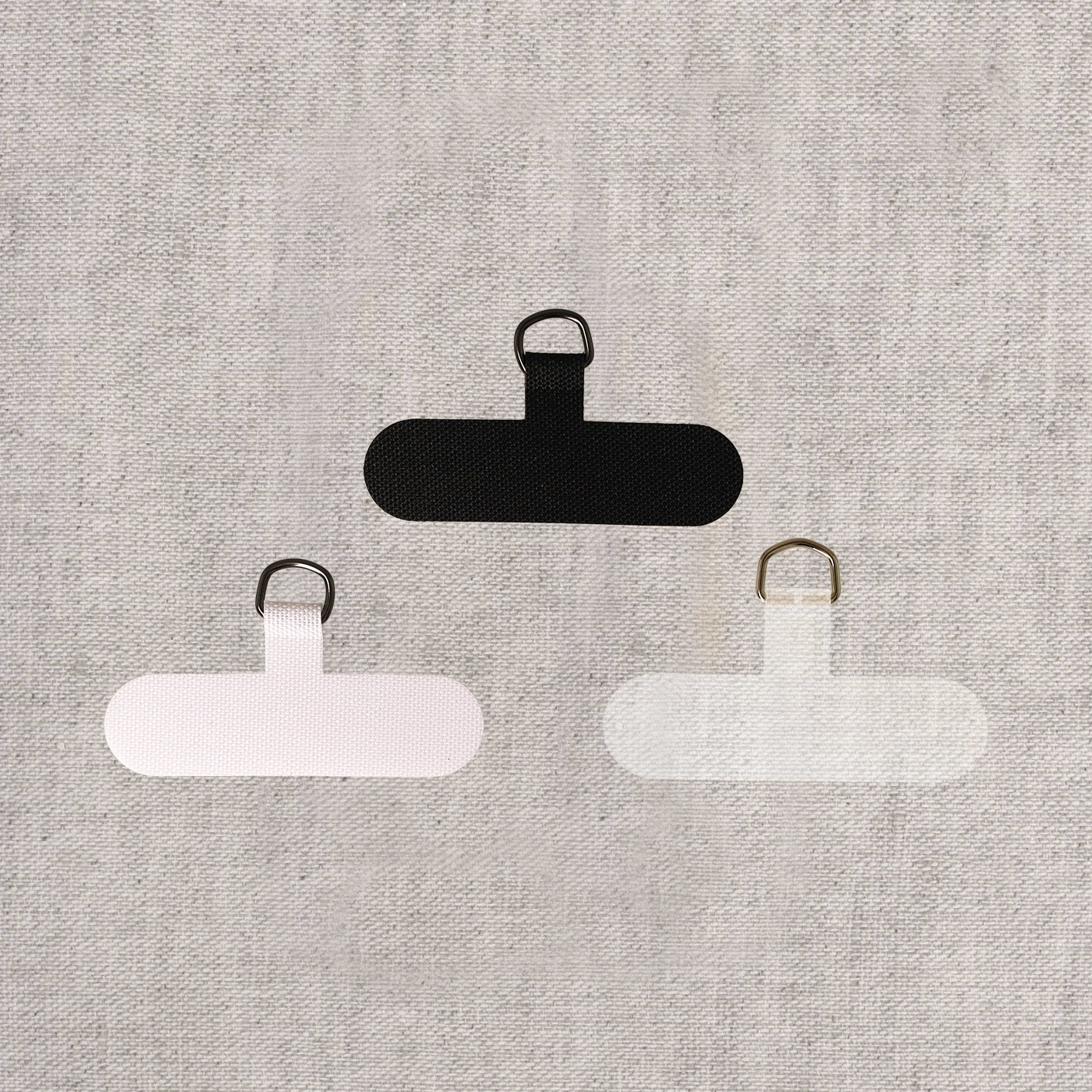 Three phone lanyard adapters in black, white, and clear with gold alloy D-rings.