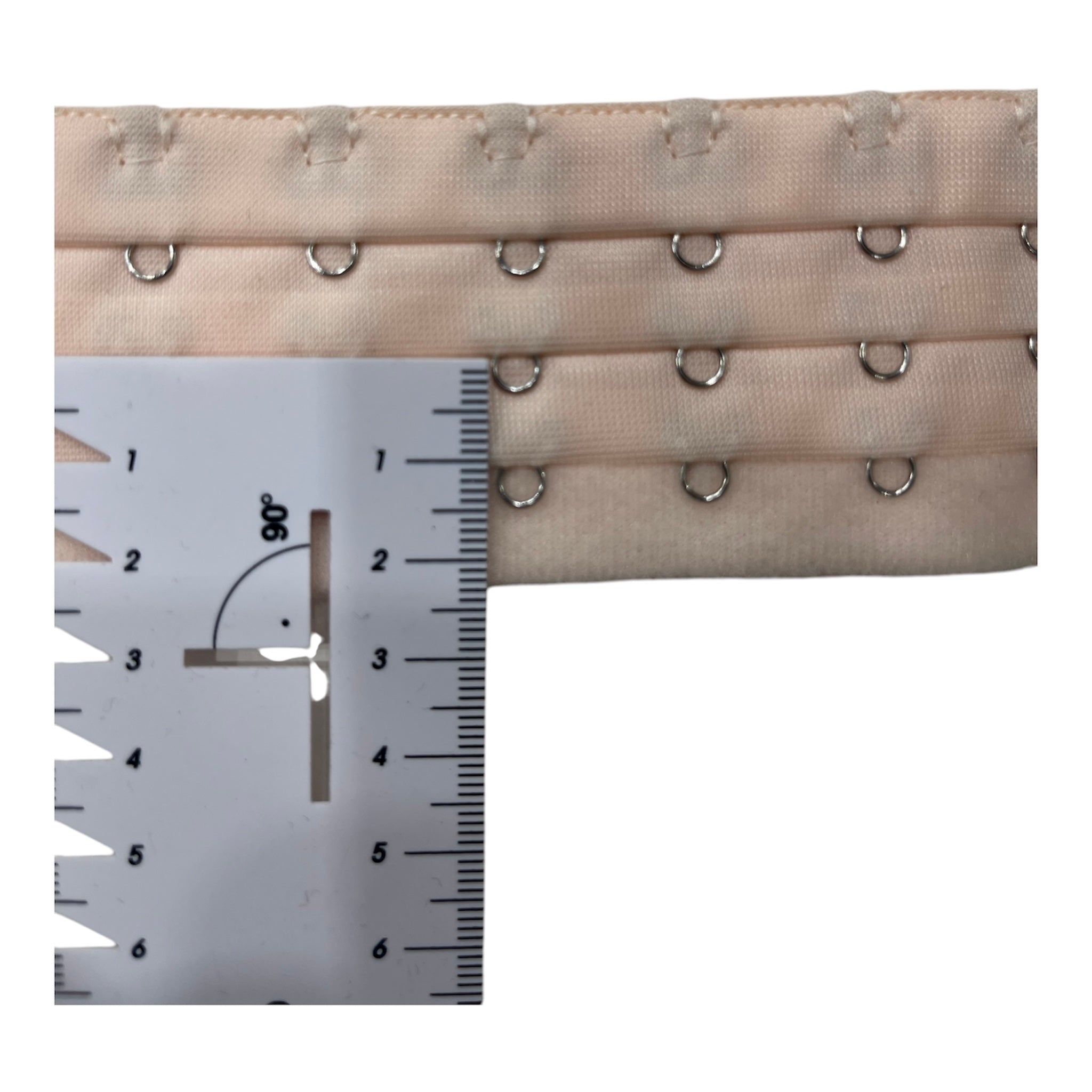 Nude polyester bra extender with three rows of hooks and eyes, measured with a ruler.