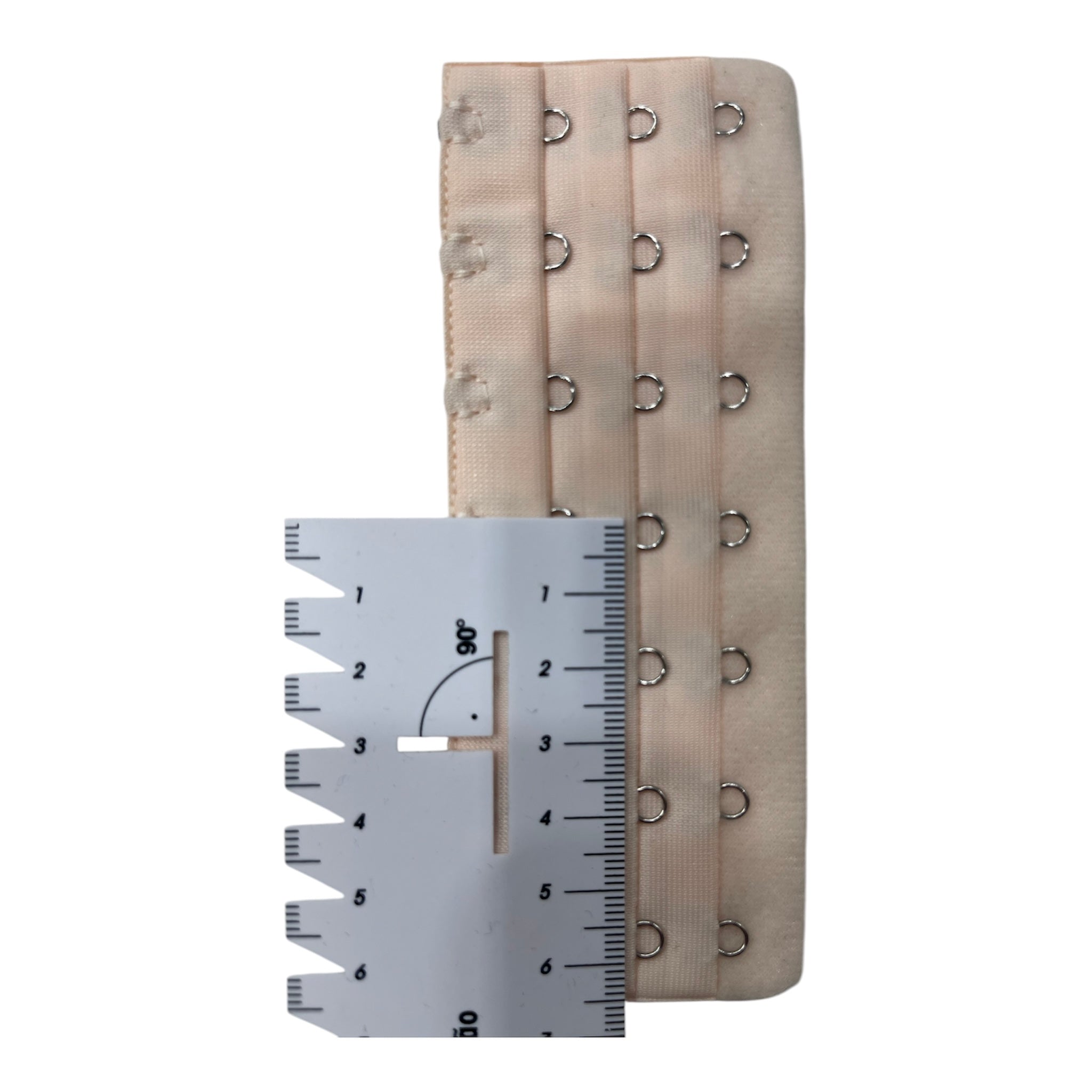 Nude polyester bra extender with multiple hook and eye closures, measured with a ruler.