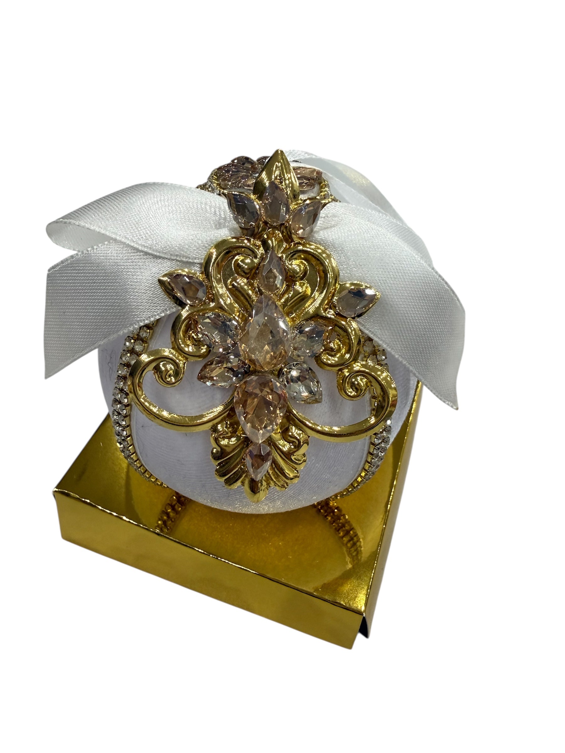 Round white ornament with gold and jewel embellishments on a gold box.
