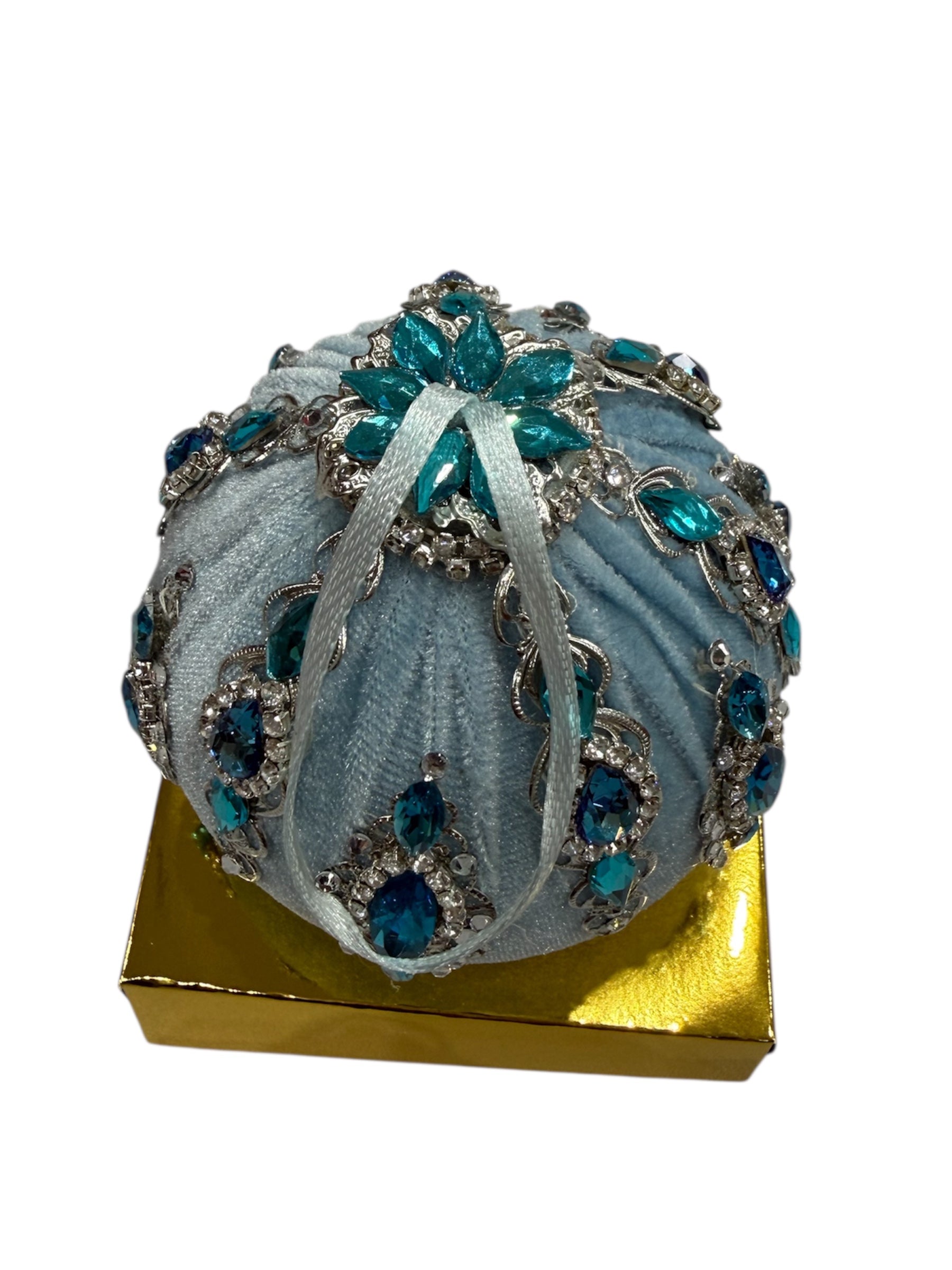 Round light blue hand-embroidered ornament with teal jewels on a gold box.