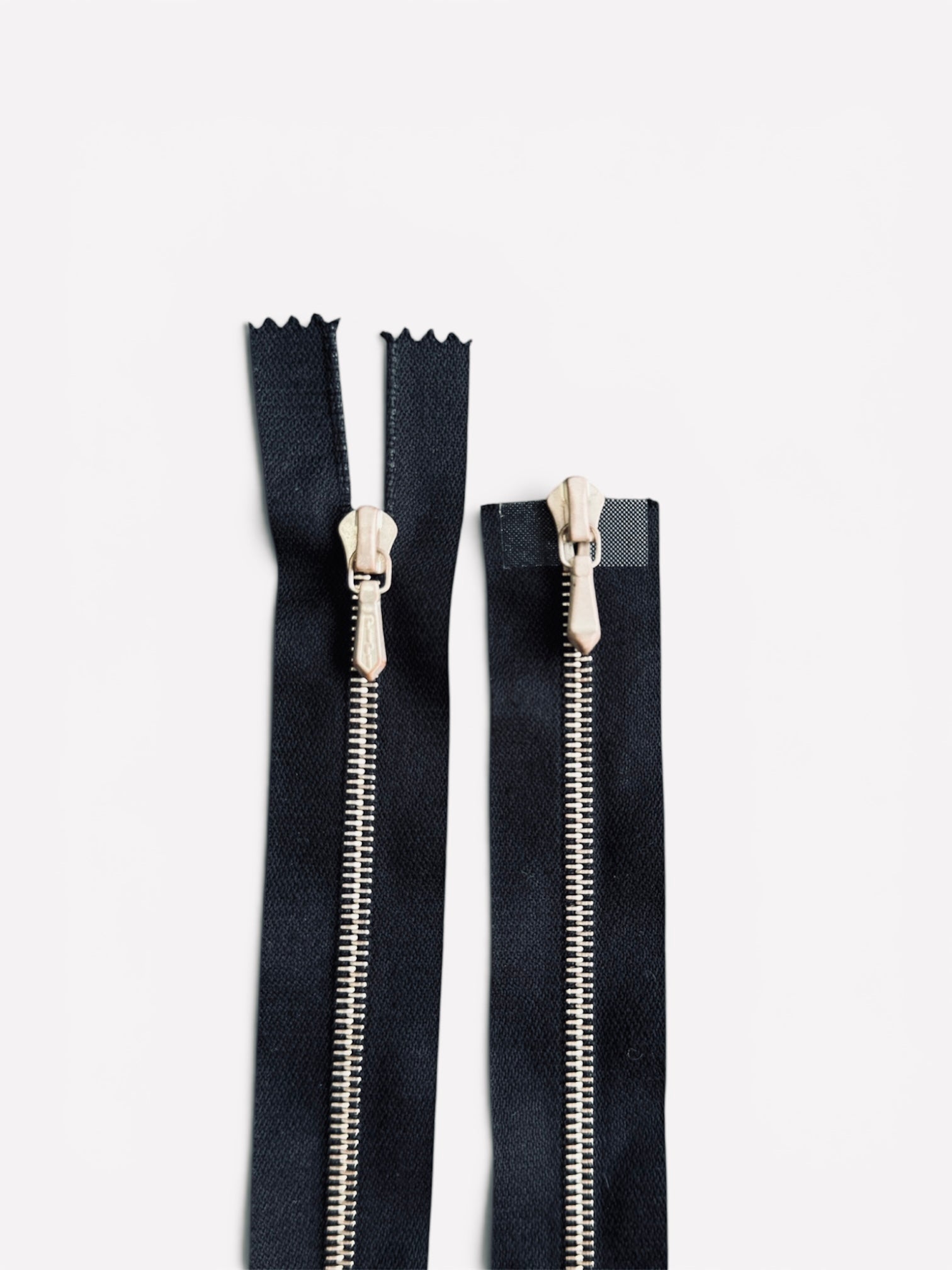 Two black Riri metal zippers with rose gold teeth and sliders against a white background.