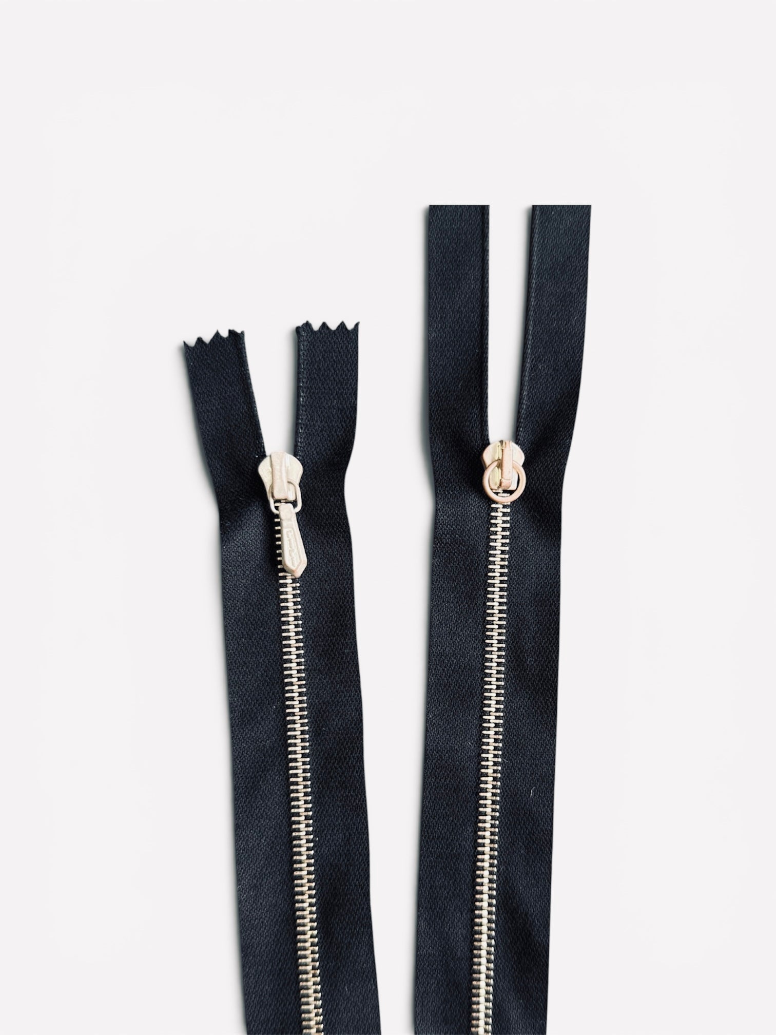 Two Riri 65cm two-way metal zippers with black tape and rose gold teeth on a white background.