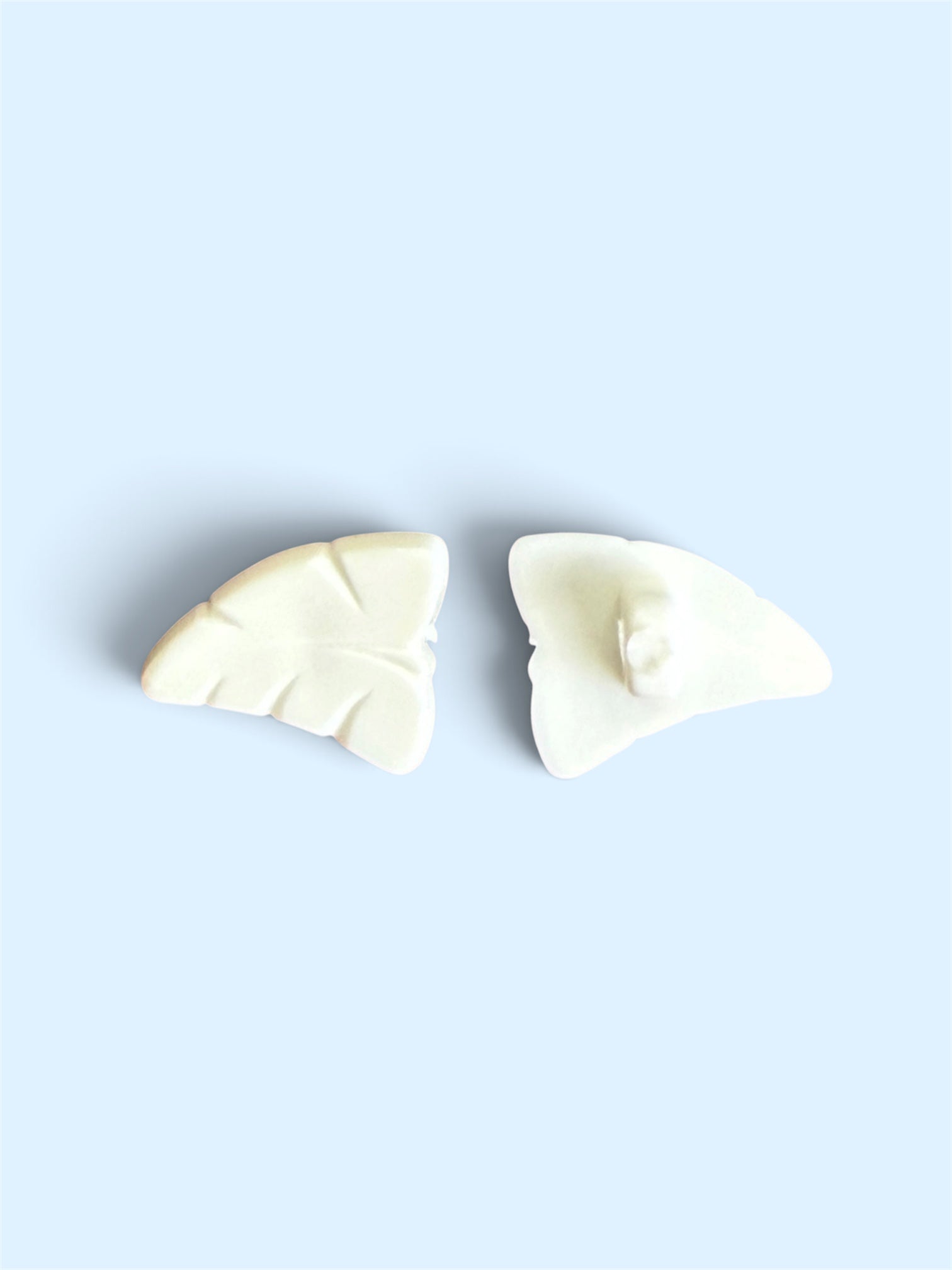 Two 12mm white leaf-shaped buttons with carved vein details on a light blue background.