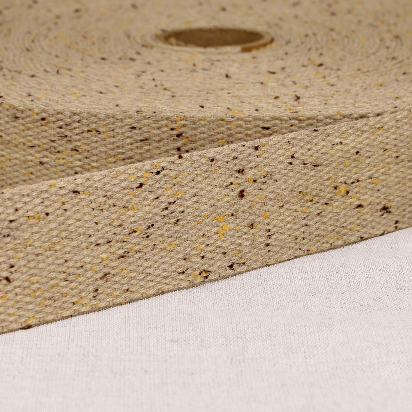 A roll of 20mm mottled beige polyester webbing strap with brown and yellow flecks.