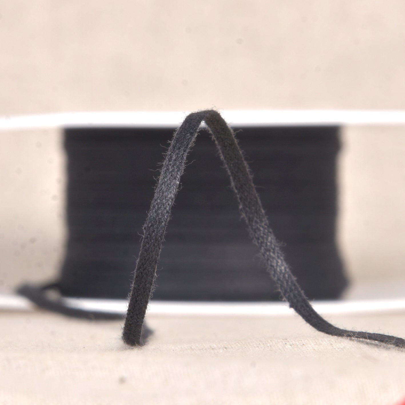 A close-up of black 3mm cotton draping tape on a spool for garment patterning.