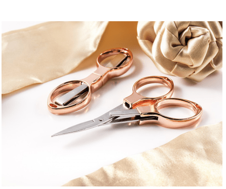 Rose gold folding scissors with silver blades, shown with satin fabric.