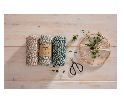 Three spools of twisted craft yarn in beige, green, and white on a wooden surface.