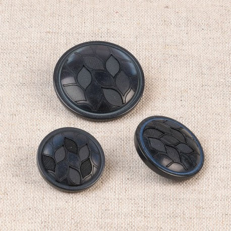 Three black polyester shank buttons with a textured leaf design in various sizes on a beige fabric.