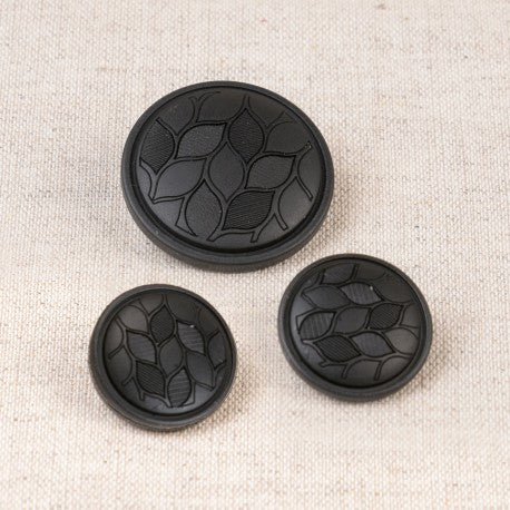 Three black polyester shank buttons with an embossed leaf pattern in varying sizes on a beige fabric.