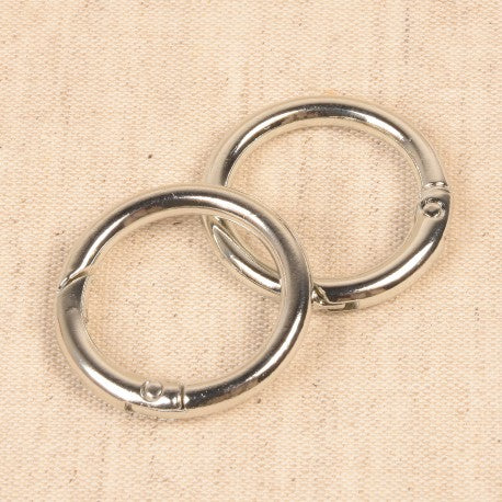 Two silver-colored round metal spring gate clips for bags on a neutral fabric background.