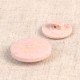 Two light pink, round eco-friendly rice husk and polyester buttons on a textured beige surface.