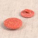 Two round, textured orange buttons made from rice husk and polyester shown on a neutral background.