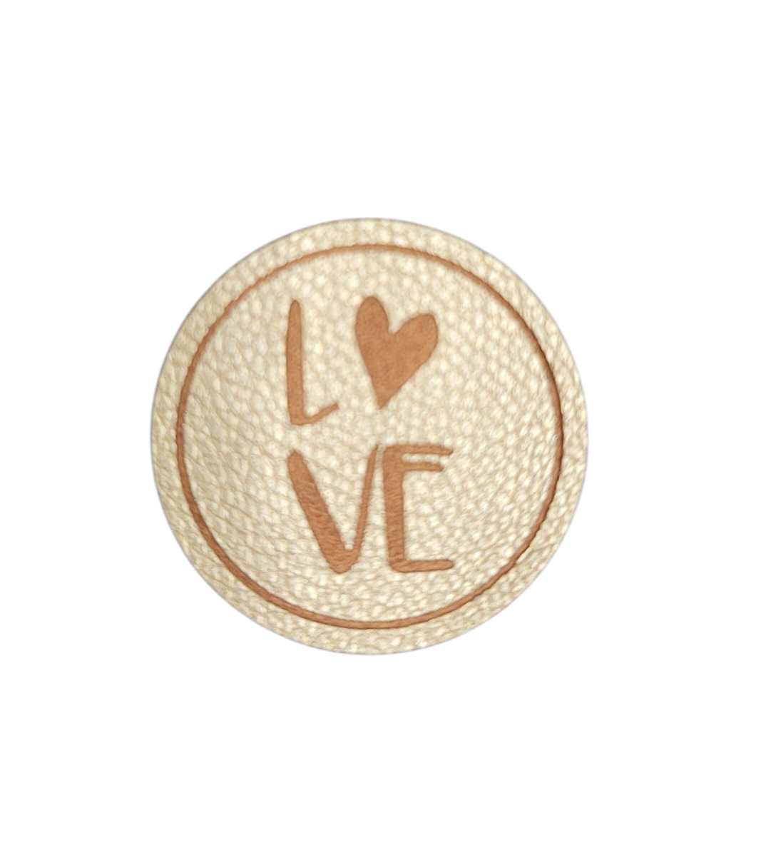 A round, cream-colored leather iron-on patch with an embossed brown LOVE design and heart.