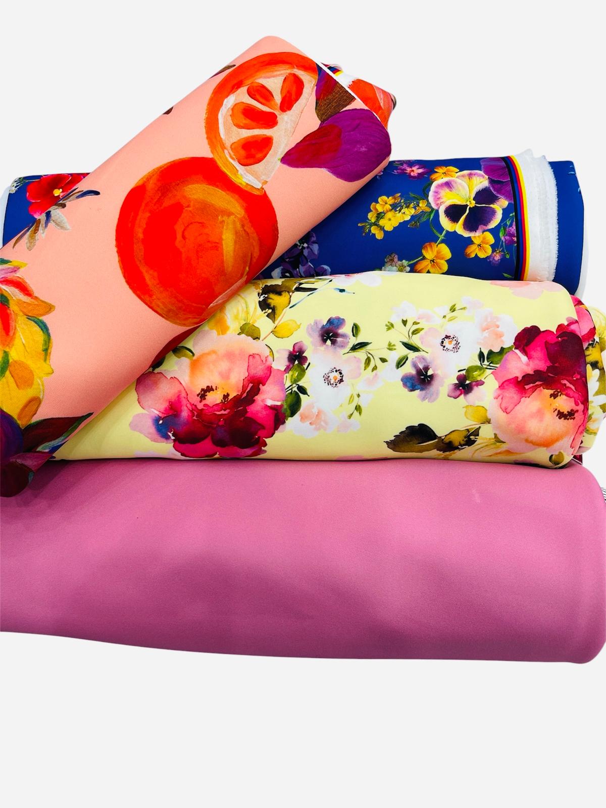 A stack of four colorful fabric rolls featuring various floral, citrus, and solid pink patterns.