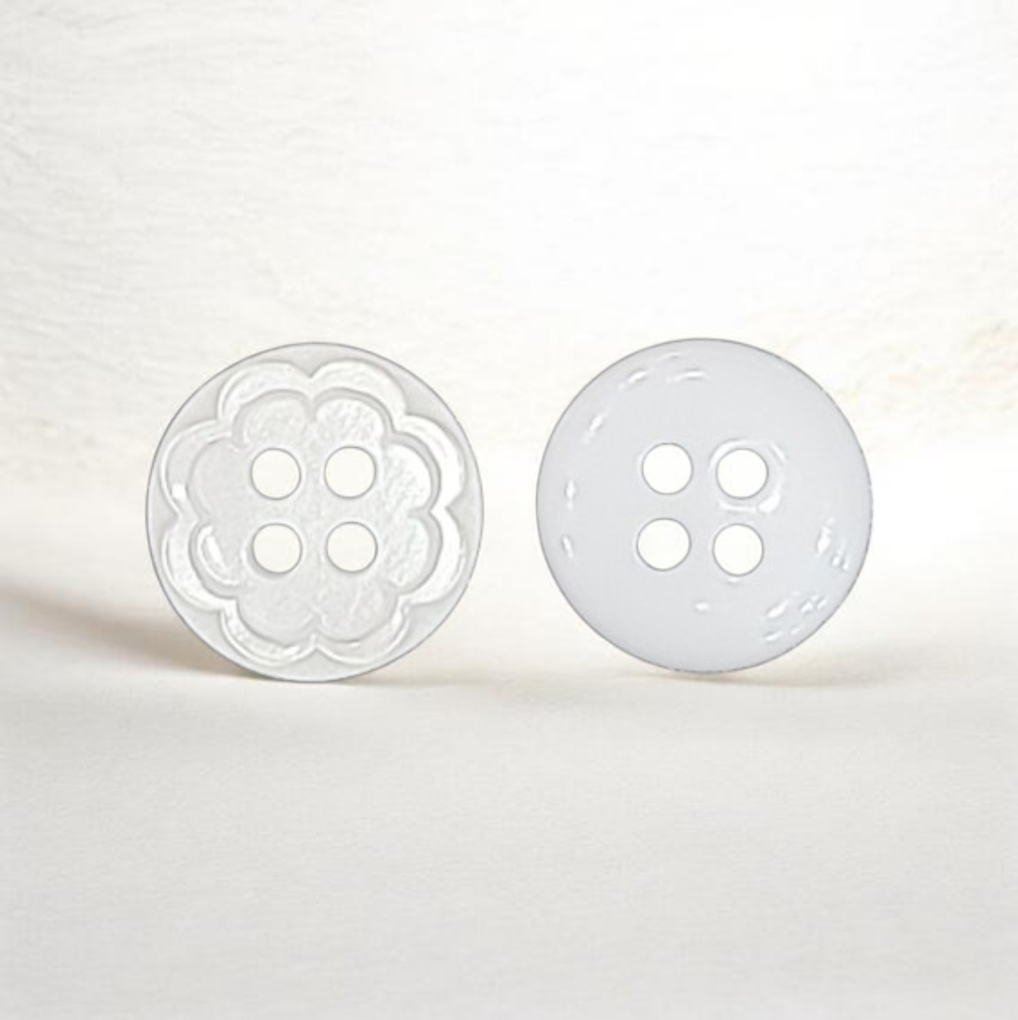 White 12mm plastic sewing button with a flower design, four holes, front and back.