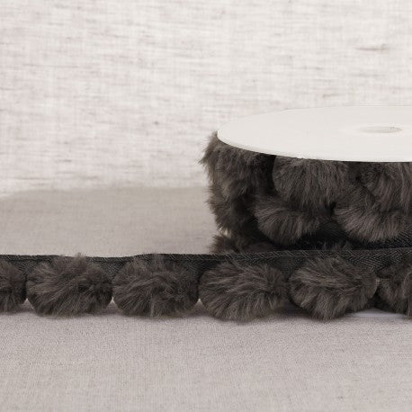 Stephanoise dark grey synthetic fur pompom trim on a spool and laid out on a neutral surface.
