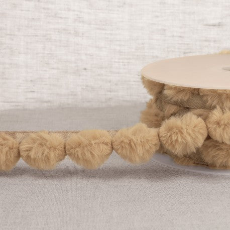 A roll of tan synthetic fur pompom trim made of polyester craft fringe.