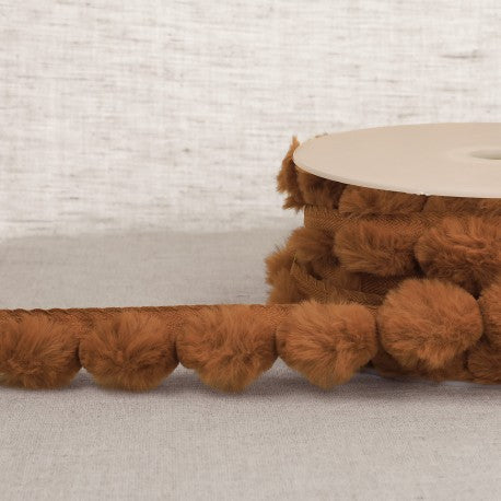 Stephanoise synthetic fur pompom trim in a warm brown color wound around a spool.