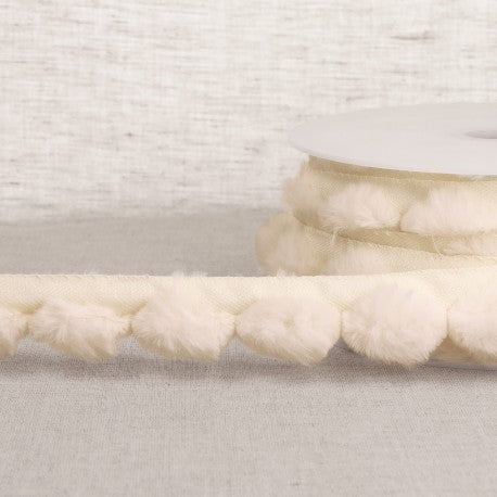 Cream-colored synthetic fur pompom trim on a spool for craft and sewing projects.