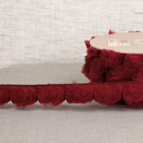 A spool of deep red synthetic fur pompom trim made of 100% polyester for craft projects.