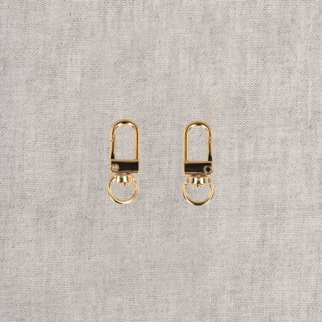 Two gold-colored metal swivel hook clips are shown side-by-side on a grey textured background.